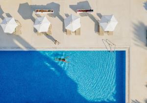 eine Aussicht auf einen Mann, der in einem Pool mit weißen Sonnenschirmen schwimmt in der Unterkunft Louis Imperial Beach in Paphos City