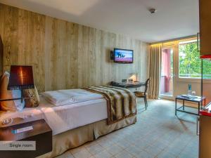 a bedroom with a bed and a desk and a television at Grischa - Das Hotel Davos in Davos