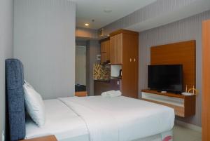 a bedroom with a white bed and a flat screen tv at Comfortable Studio Grand Kamala Lagoon Apartment By Travelio in Pekayon Satu