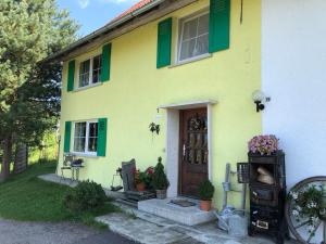 une maison jaune avec des volets verts et une porte dans l'établissement Weiher 1, à Rot an der Rot