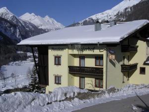 a building covered in snow with mountains in the background at Pension Trojerhof in Heiligenblut