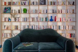 a green couch in front of a book shelf with books at Chouchou Hotel in Paris