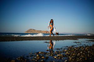 Alkionides Seaside Hotel في بلاتانياس: امرأة تمشي على الشاطئ مع لوح ركوب الأمواج