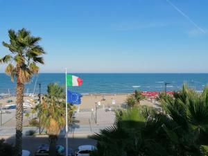 a beach with a flag and palm trees and the ocean at Residence Le Palme in Grottammare