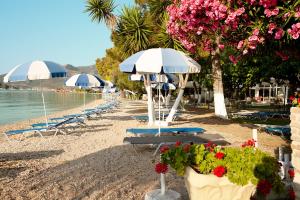 ein Strand mit Stühlen, Sonnenschirmen und Blumen in der Unterkunft Avra Beach Hotel in Nydri