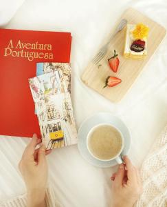 a person holding a cup of coffee next to a book at New! Nice FAMILY Apartment with 2 Bedroom, 2 Terrace in Costa da Caparica