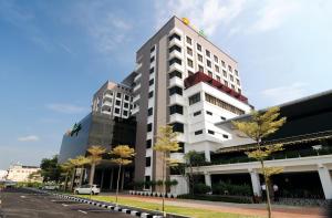 a tall white building with trees in front of a street at Kings Green Hotel City Centre Melaka in Malacca