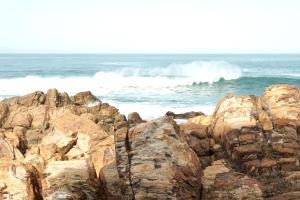 un grupo de rocas en el océano con olas en The Point Hotel & Spa, en Mossel Bay