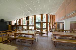 a classroom with wooden tables and benches and windows at Auberge de Jeunesse HI Séez in Séez