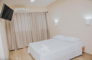 1 dormitorio con 1 cama blanca y TV de pantalla plana en Pousada La Brisa en Itaguaí