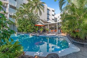 a swimming pool with palm trees and a building at Amaroo At Trinity in Trinity Beach