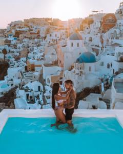 un hombre y una mujer de pie en la cima de una piscina con vistas a una ciudad en Aspaki by Art Maisons, en Oia