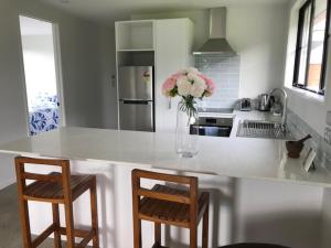 a kitchen with a counter with two chairs and a vase of flowers at Lakin' it easy Cottage in Karapiro