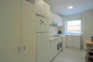 cocina con armarios blancos y nevera blanca en Apartamento CasaTuris enfrente al mar en Playa Muchavista C102, en El Campello