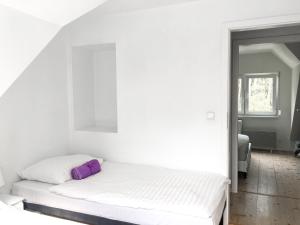 ein weißes Schlafzimmer mit einem Bett mit einem lila Kissen in der Unterkunft Lawendowe Domki Dziwnówek in Dziwnówek