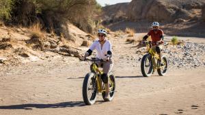 two people riding bikes on a dirt road at Wilderness Safaris Kulala Desert Lodge in Sesriem