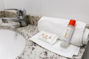 a bathroom sink with a towel and a bottle of sunscreen at Hotel Expressinho Aeroporto in Porto Alegre
