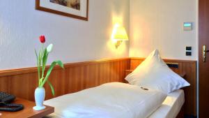 una habitación de hotel con una cama y un jarrón con una flor en Hotel Ilbertz Garni en Colonia
