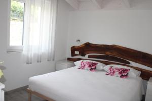 a white bedroom with a white bed with pink pillows at Agriturismo Nona Emma in Piano Porlezza