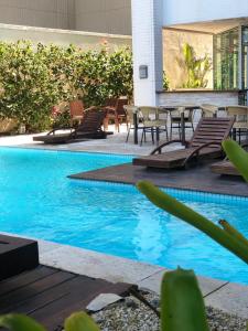 a swimming pool with chairs and a table and blue water at Mandai Apartamentos in Cabo Frio
