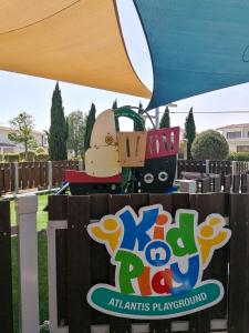 a sign for a playground with a train on it at Atlantis Gardens in Mazotos