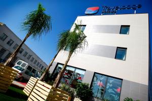 un bâtiment blanc avec des palmiers devant dans l'établissement Travelodge Valencia Aeropuerto, à Manises