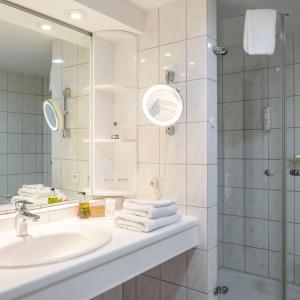 a bathroom with a sink and a shower with a mirror at Ringhotel Hohe Wacht in Hohwacht