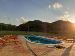 a swimming pool with chairs and the sun in the background at Pensiunea Agroturistica Green Odoba in Sătuc
