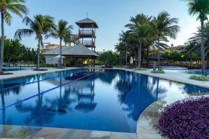 a large swimming pool with palm trees and a tower at Golf Ville Resorts Suites in Aquiraz