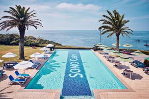 een zwembad met stoelen en palmbomen en de oceaan bij Sono Calm Jeju in Seogwipo