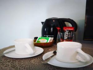 two white cups and saucers on a table with a coffee pot at The Guest Chang Moi Hotel in Chiang Mai
