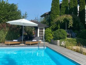 a swimming pool with an umbrella and two chairs at Landhaus am Plattenbichl - Luxus Apartment mit Pool und Sauna - im Sommer Bergbahn inklusive in Oberstdorf +20 photos