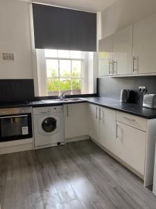 uma cozinha com armários brancos e uma máquina de lavar e secar roupa em Union Street Apartment em Hawick