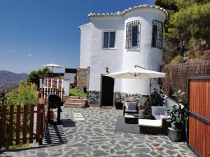 a white house with a fence and chairs and an umbrella at Casa Ayo in Frigiliana
