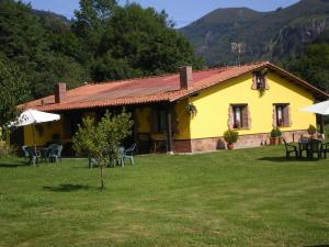 ein gelbes Haus mit Tischen und Stühlen im Hof in der Unterkunft Apartamentos Rurales El Buxu in Soto de Cangas