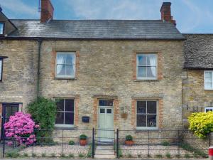 an old brick house with a green door and pink flowers at Rathbone Cottage in Stow on the Wold