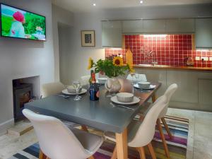 a dining room table with white chairs and a television at Rathbone Cottage in Stow on the Wold