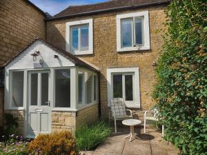 a house with a door and a chair and a table at Woodbine Cottage in Bourton on the Water