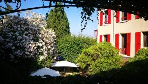 Hôtel Les Orangers في هييريس: مبنى به مصاريع حمراء وحديقة بها زهور
