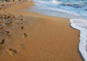 a beach with footprints in the sand and water at Galini Palace in Athens