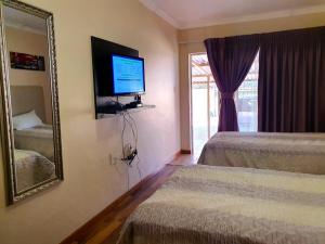 a bedroom with two beds and a mirror and a television at Tenacity Guesthouse - Riviera Park in Mahikeng