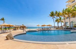 a swimming pool at a resort with palm trees and the ocean at Villa del Palmar Beach Resort & Spa Puerto Vallarta in Puerto Vallarta