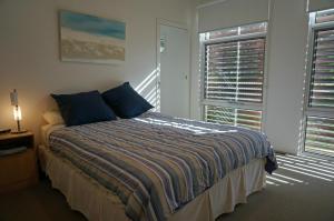 a bedroom with a bed with blue pillows and two windows at Baillieu Breeze in Point Lonsdale