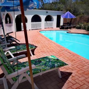 a swimming pool with two lounge chairs and an umbrella at Phantom Croft Guest Lodge in Mossel Bay