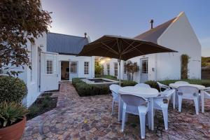 a patio with white tables and chairs and an umbrella at The Vishuis in Hermanus