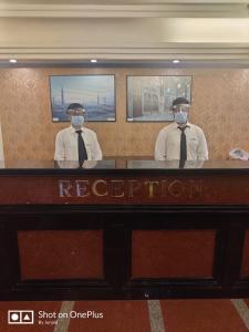 deux hommes portant des masques pour le visage sur un bureau d'un hôtel dans l'établissement Hotel Mogul Palace - Near CST Station, à Mumbai