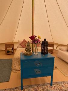 a blue nightstand with a vase of flowers on top of a bed at Swallows Oast Glamping in Sedlescombe +23 photos