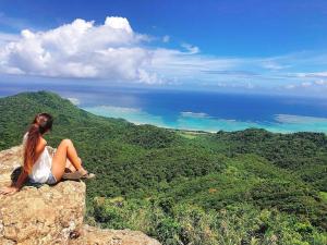 a woman sitting on top of a rock looking at the ocean at guest house Holoholo Ishigakijima in Ishigaki Island