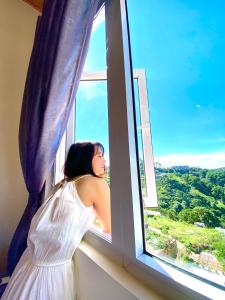 uma mulher num vestido branco a olhar pela janela em Sweet Dream Hotel & Villa em Da Lat