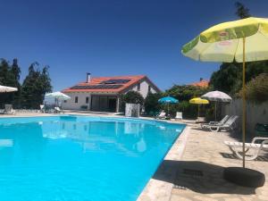 una gran piscina con sombrilla y sillas en Quinta das Cegonhas, en Gouveia